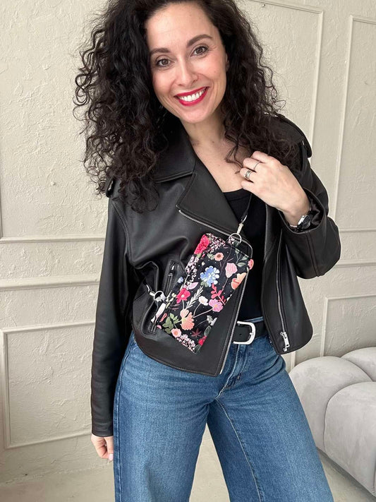 Käsintehty puhelinlaukku, jossa on mustalla pohjalla värikkäitä kukkia sekä säädettävä hihna. Laukkuun mahtuu puhelin, passi ja useita kortteja.