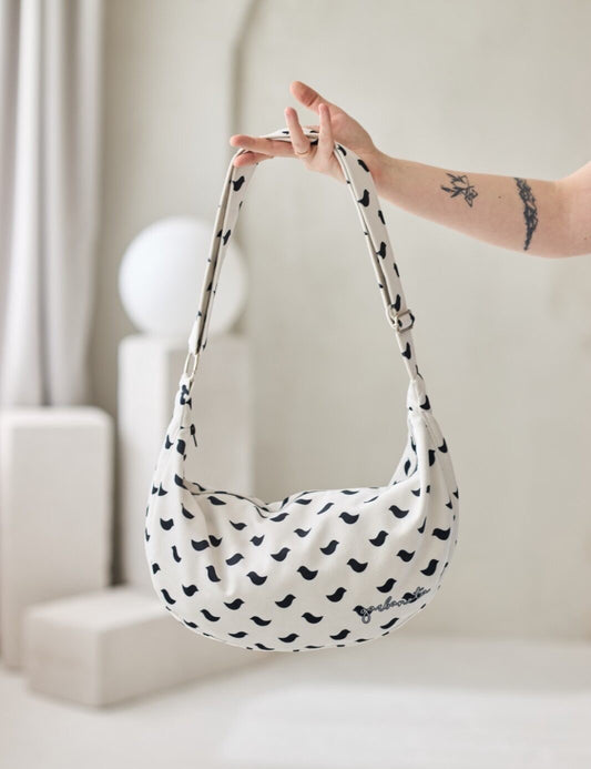 Garbanota -tuotemerkin Hobo-olkalaukku, jossa mustia lintuja valkoiselle pohjalla. Valmistettu pehmeästä ja kestävästä veluurista. Garbanota -kuvioinen vuori, kaksi sisätaskua ja säädettävä olkahihna.